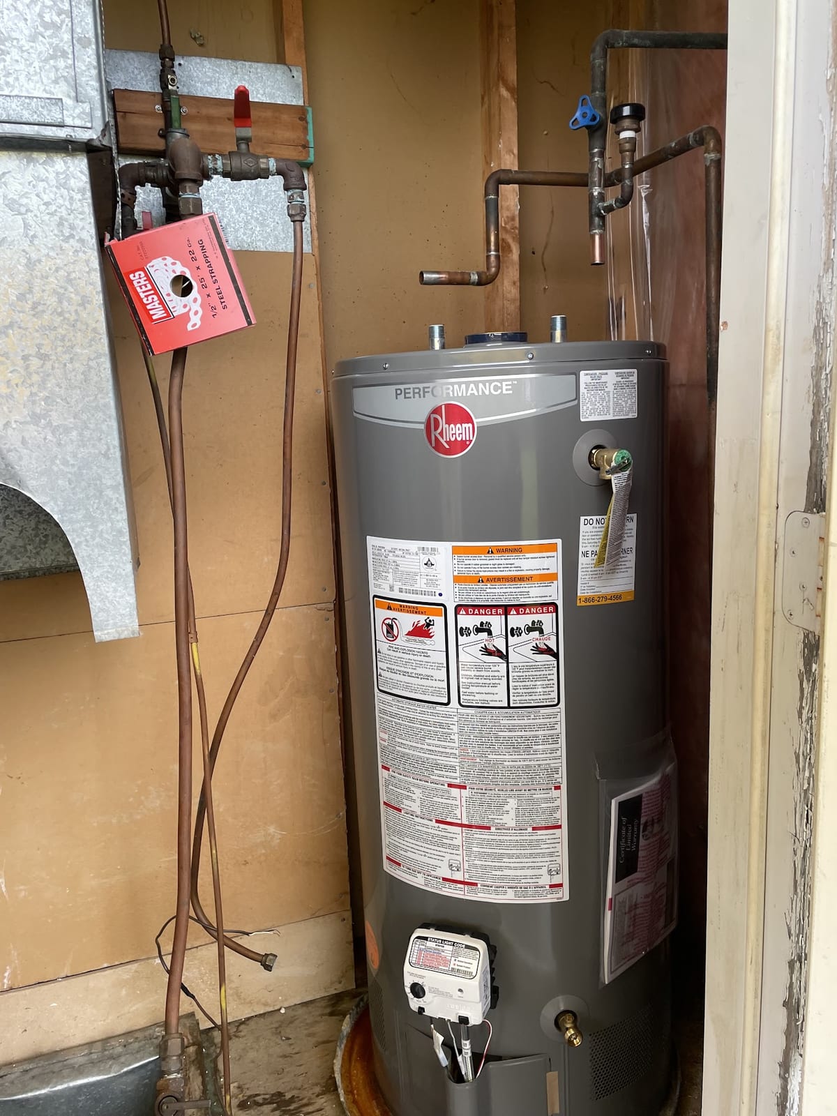Rheem Performance replacement tank positioned indoors with pipe connections unfinished